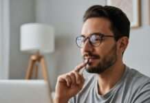 Persona reflexionando frente a una computadora en un entorno cotidiano.