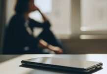 Teléfono móvil sobre una mesa en primer plano, con una figura humana desenfocada al fondo, en un ambiente de reflexión y pausa