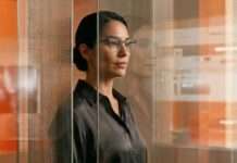 Mujer con lentes observando reflejos y elementos visuales relacionados con tecnología y autenticidad digital dentro de un entorno editorial contemporáneo.