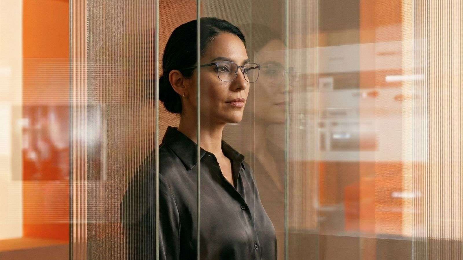 Mujer con lentes observando reflejos y elementos visuales relacionados con tecnología y autenticidad digital dentro de un entorno editorial contemporáneo.