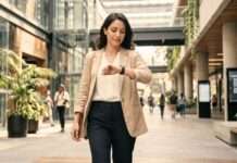 La vida digital que viene: menos pasos, más decisiones Mujer camina por un espacio urbano moderno mientras consulta discretamente su reloj inteligente.